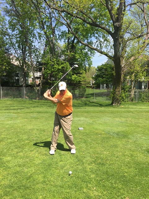 Man in orange shirt swinging golf club