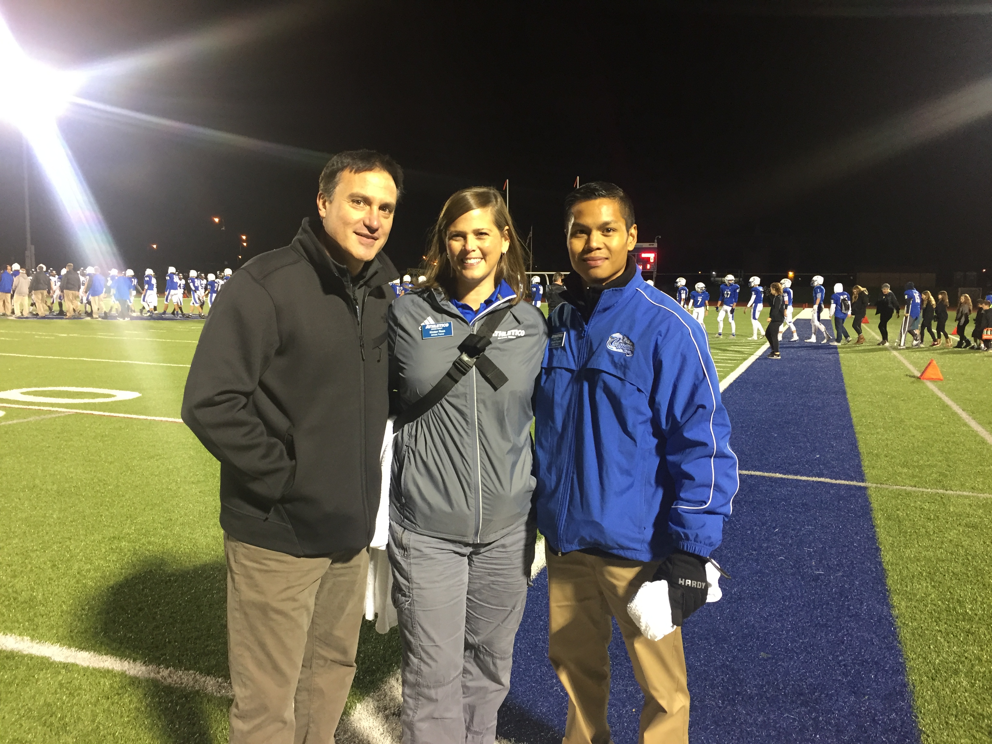Dr. Roger Chams smiling standing with man and woman on football field at night