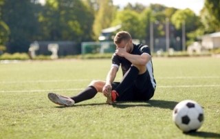 male soccer player sitting on field holding his injured foot