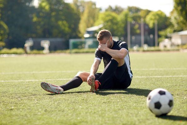 male soccer player sitting on field holding his injured foot