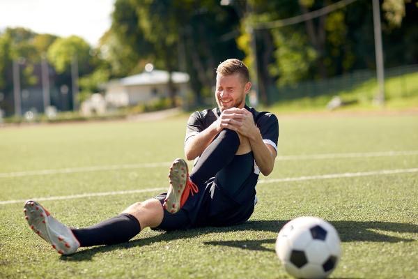 injured soccer player holding his knee on soccer field